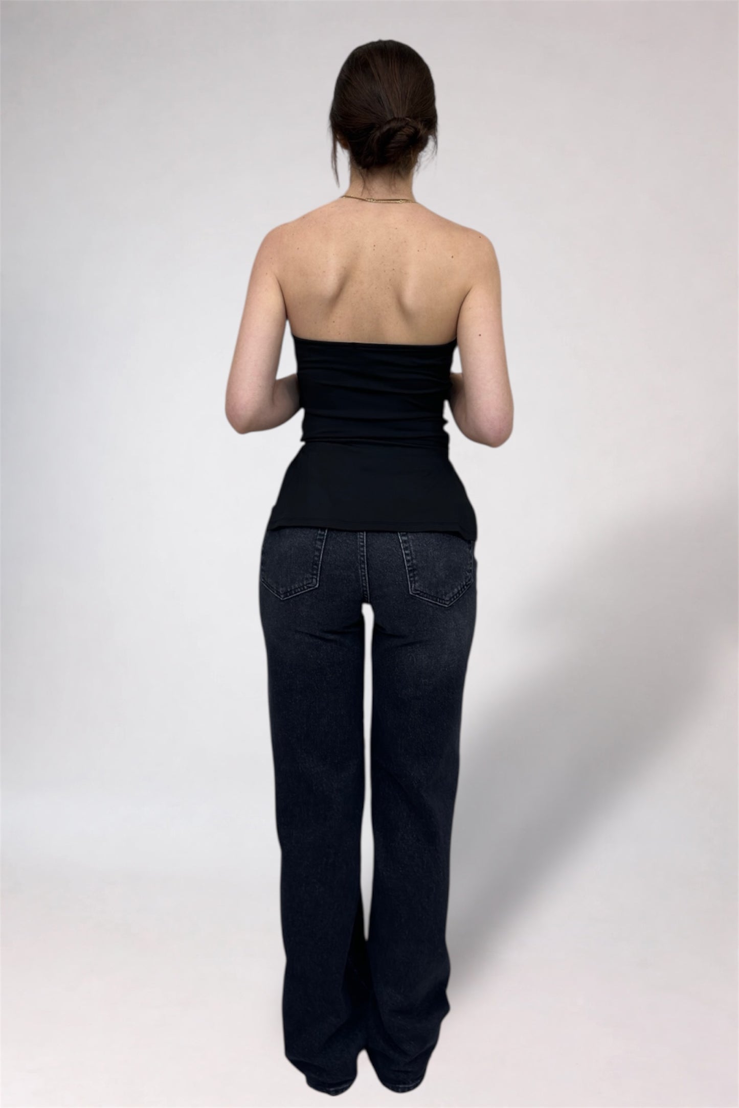 Person wearing a black strapless top and dark jeans on a white background