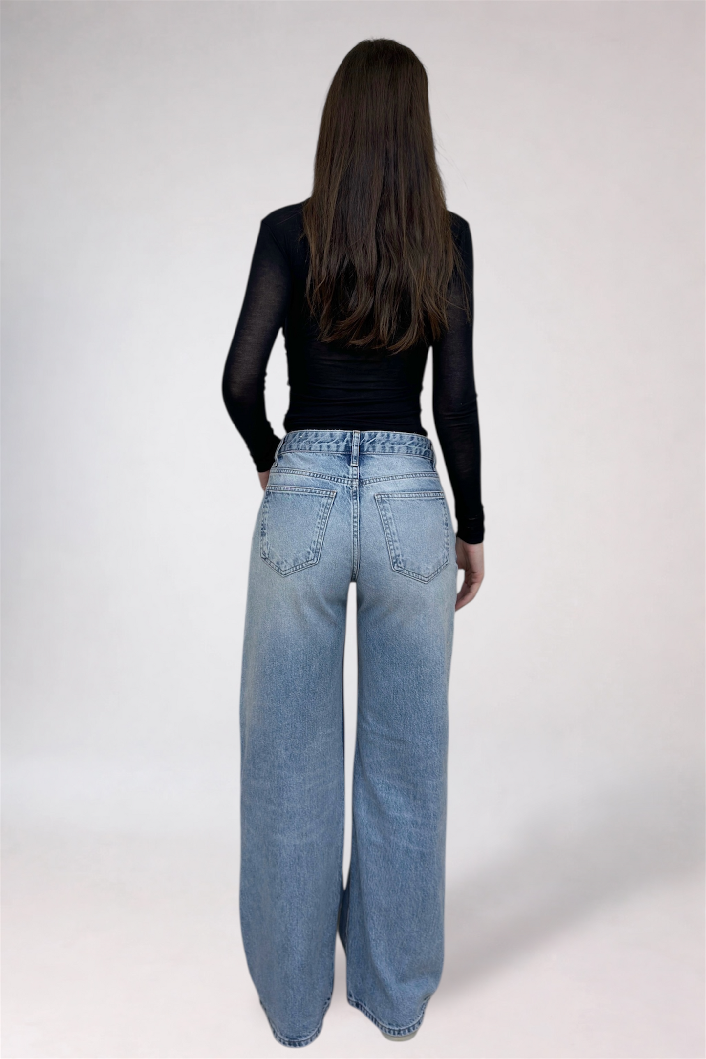 Person wearing blue jeans and a black top on a white background