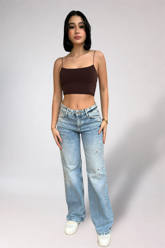 Woman wearing a brown top and blue jeans against a plain background