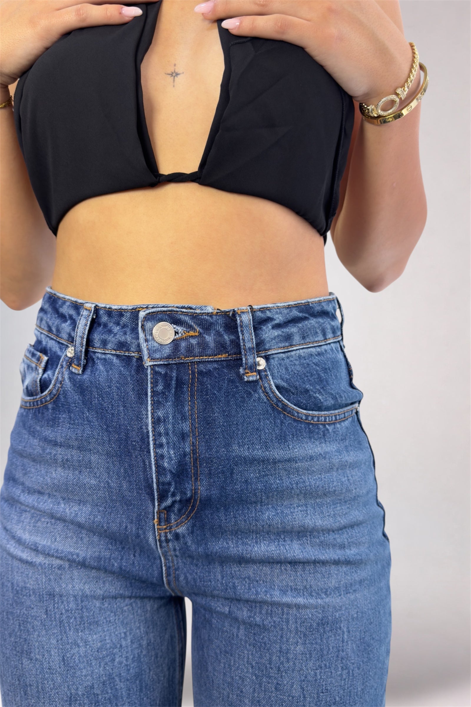 Person wearing a black crop top and blue jeans on a plain background