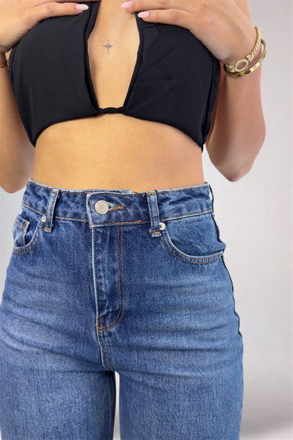 Person wearing a black crop top and blue jeans on a plain background