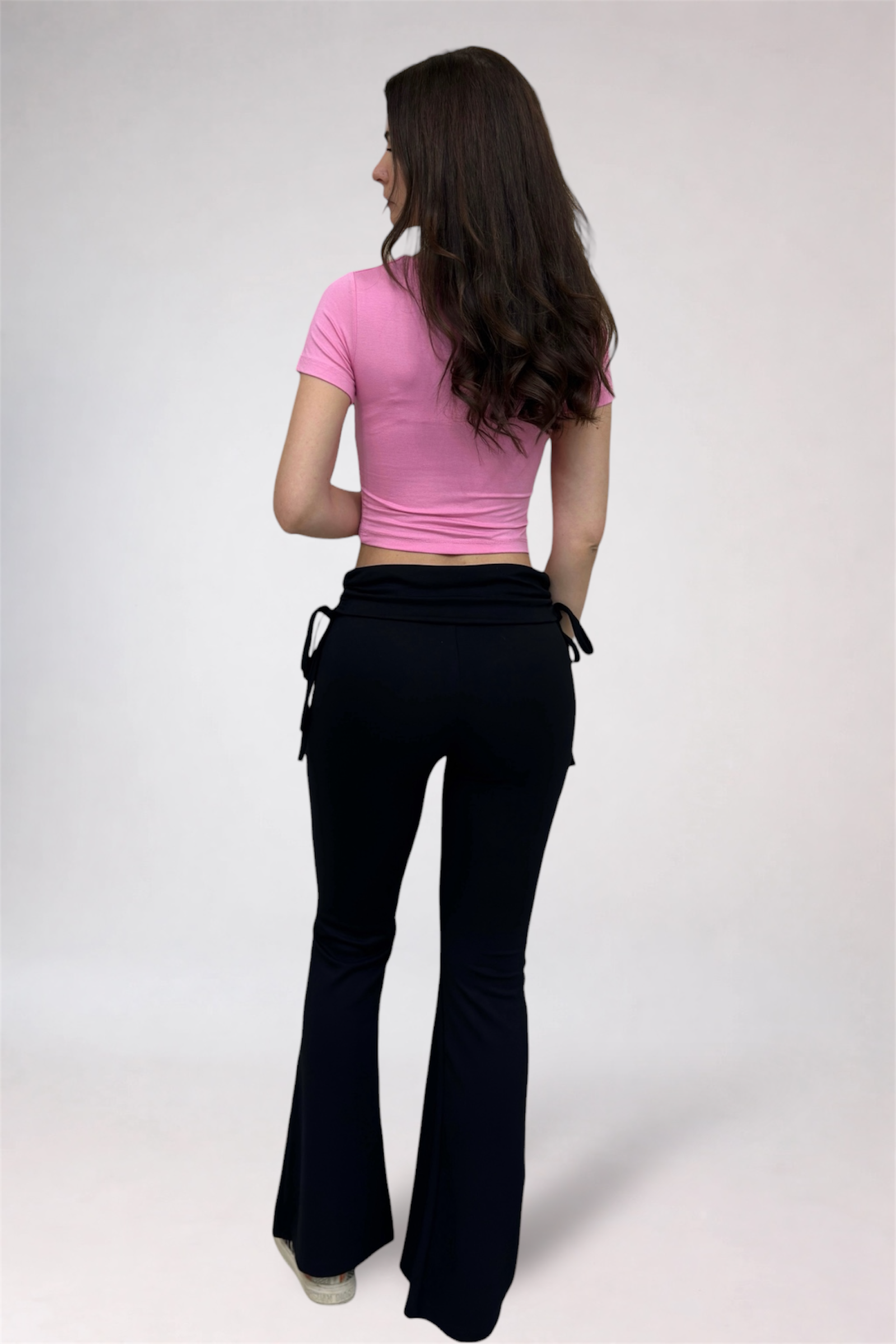 Woman wearing a pink top and black flared pants on a white background
