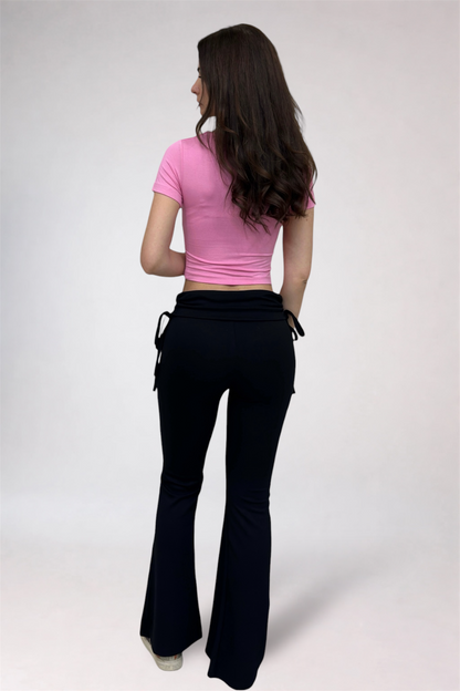 Woman wearing a pink top and black flared pants on a white background