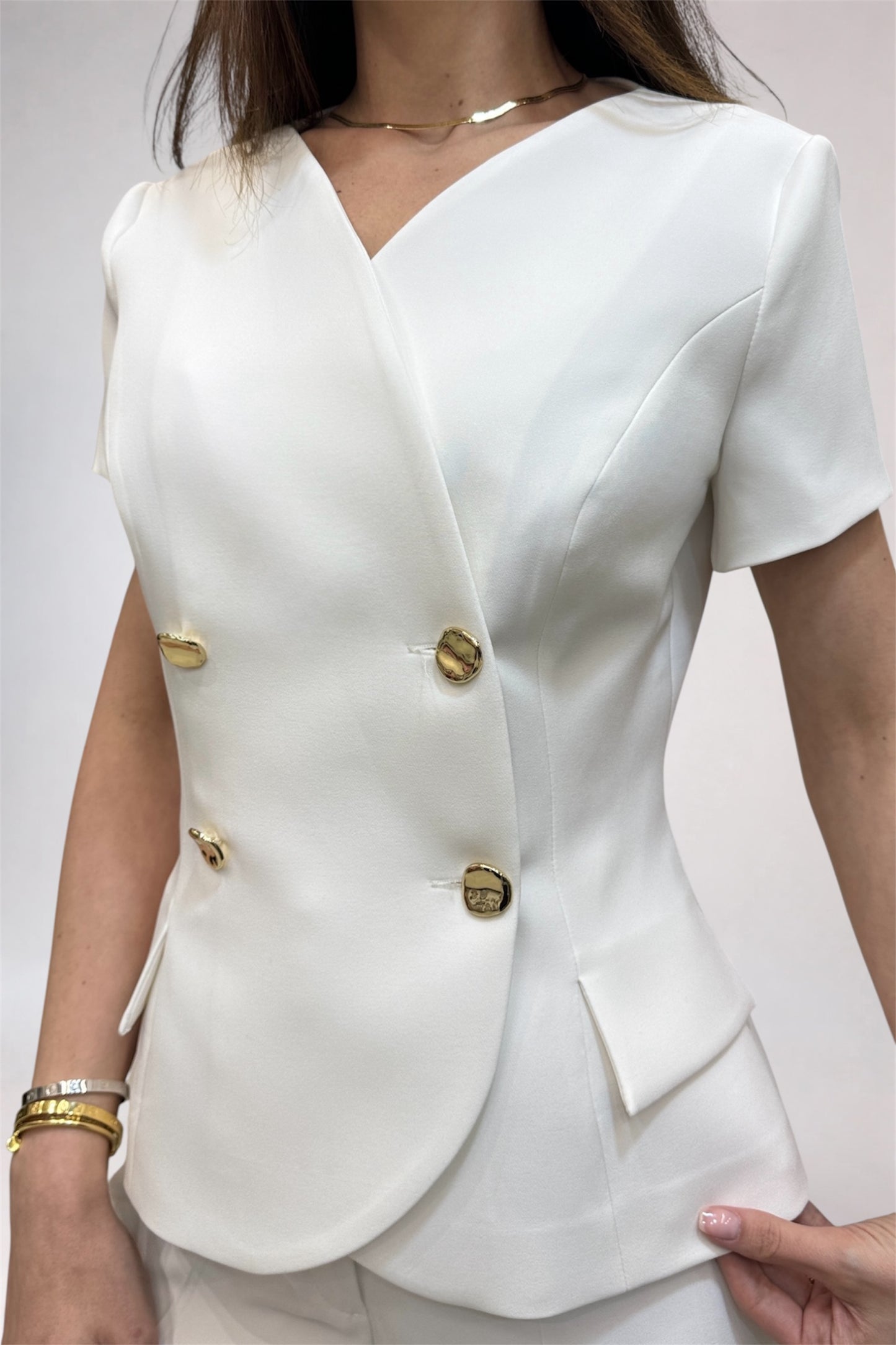 White blazer with gold buttons worn by a person on a plain background