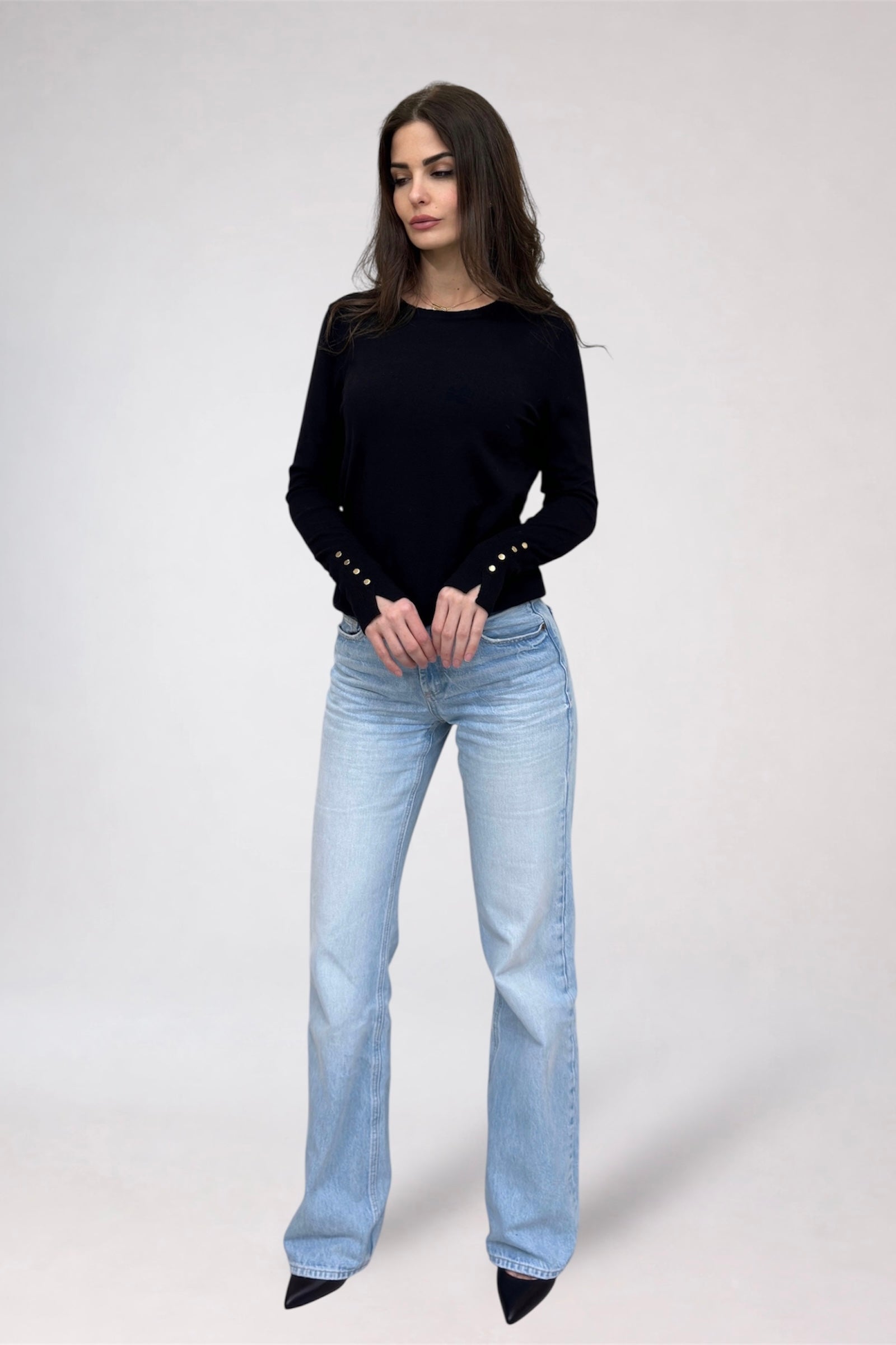 Woman wearing a black sweater with studded details and light blue jeans on a white background