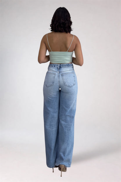 Person wearing light blue jeans and a green top on a white background