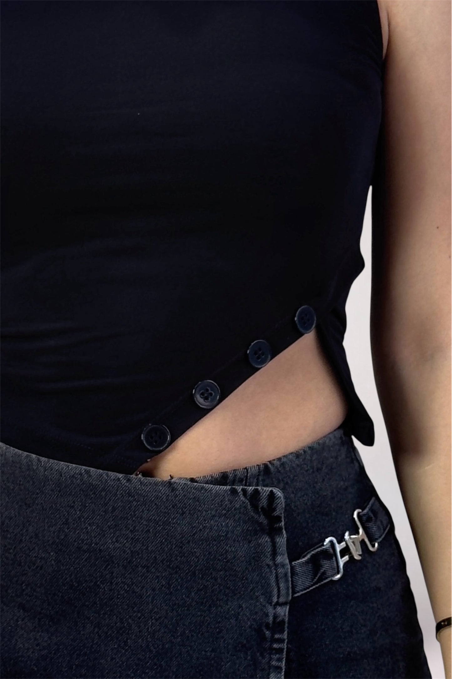 Black sleeveless top with button details worn by a person, with a blurred background.