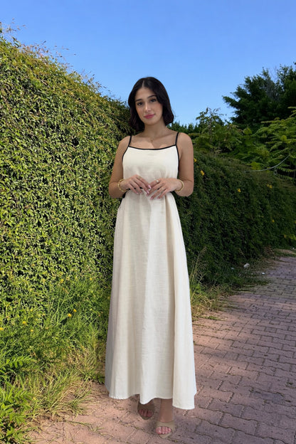 Woman in a white dress standing in front of green bushes with a clear blue sky.