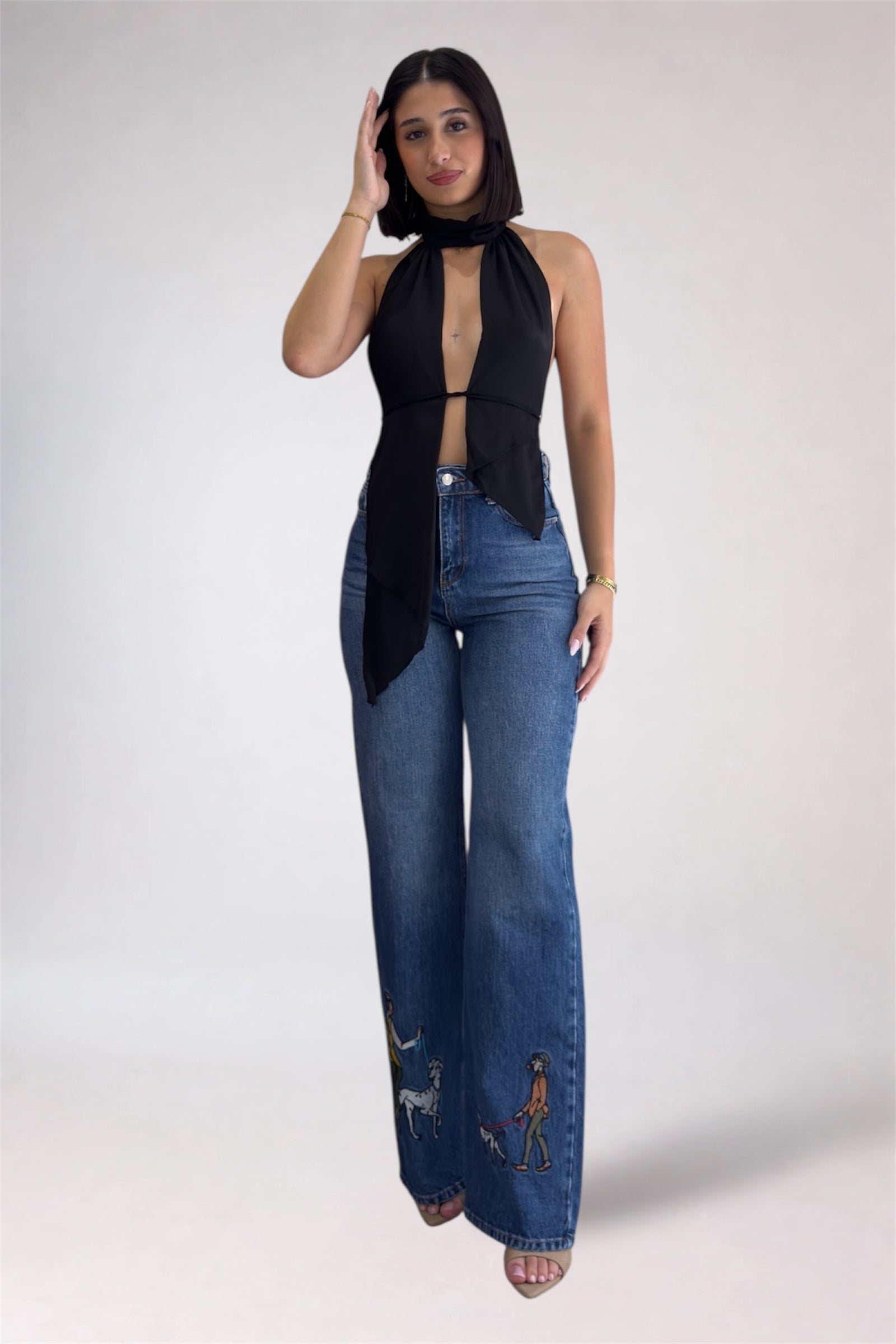 Woman wearing a black sleeveless top and blue jeans with embroidery on a white background