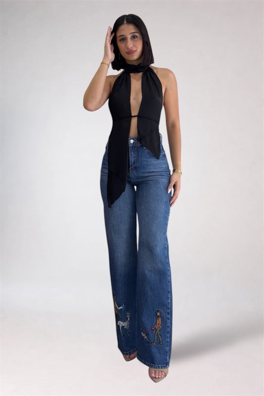 Woman wearing a black sleeveless top and blue jeans with embroidery on a white background