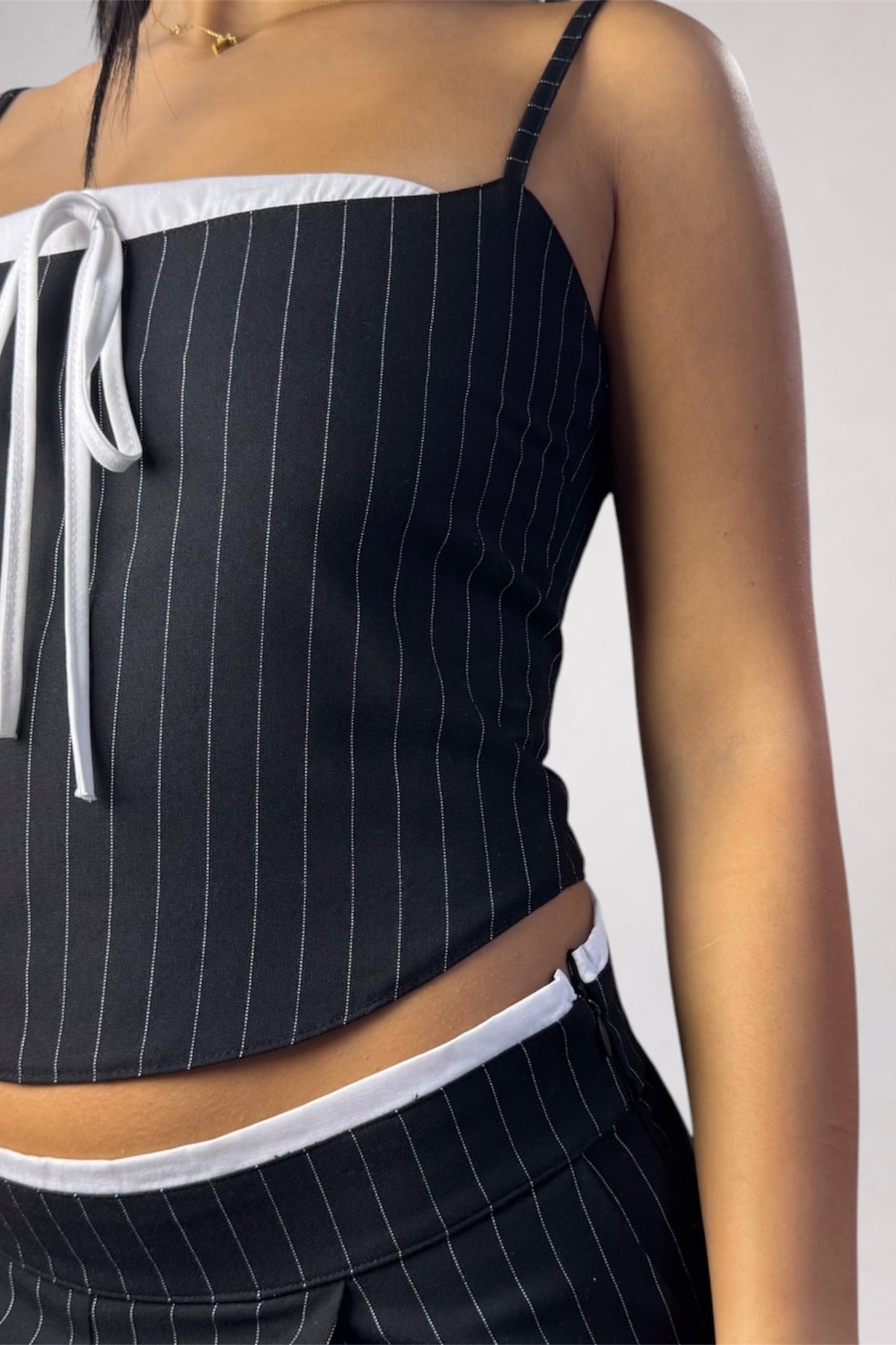 A close-up of a model wearing a black pinstriped crop top with white trim and a white tie detail, paired with matching pinstriped bottoms.