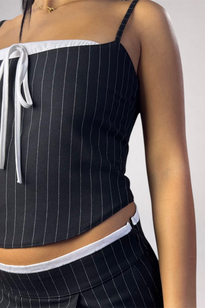 A close-up of a model wearing a black pinstriped crop top with white trim and a white tie detail, paired with matching pinstriped bottoms.