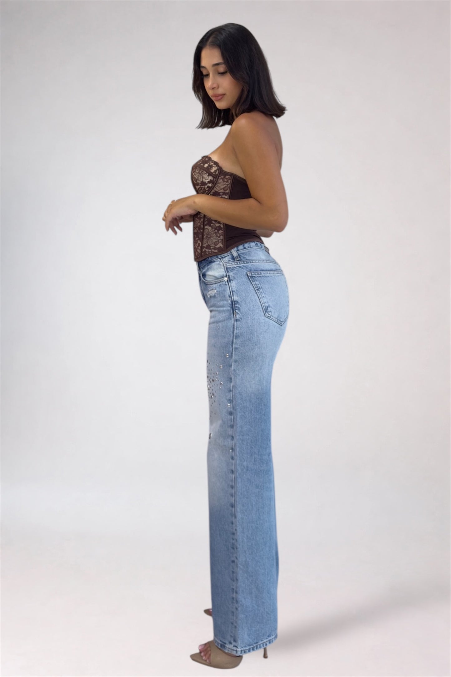 Woman wearing a lace top and light blue jeans on a white background