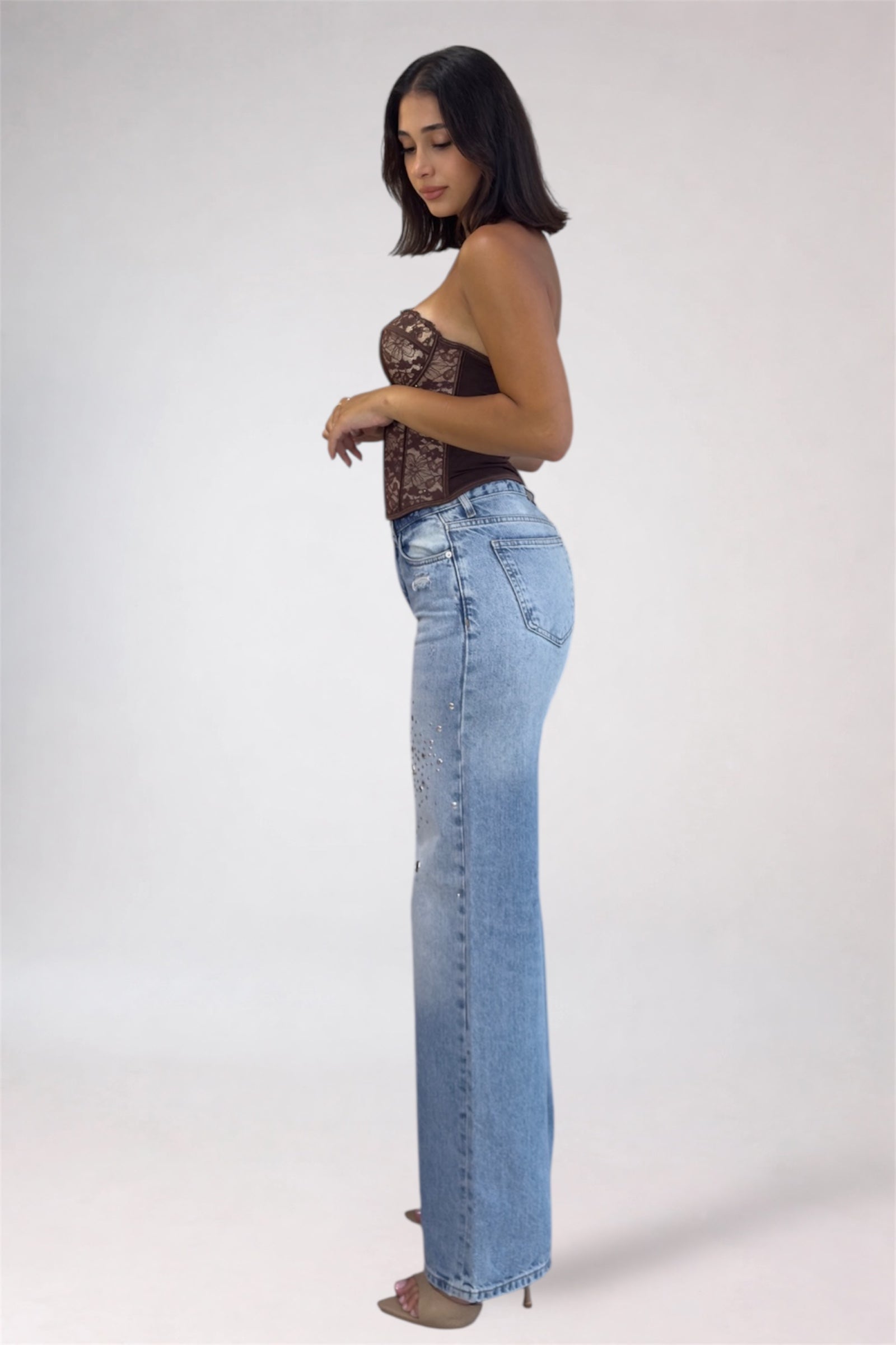 Woman wearing a lace top and light blue jeans on a white background