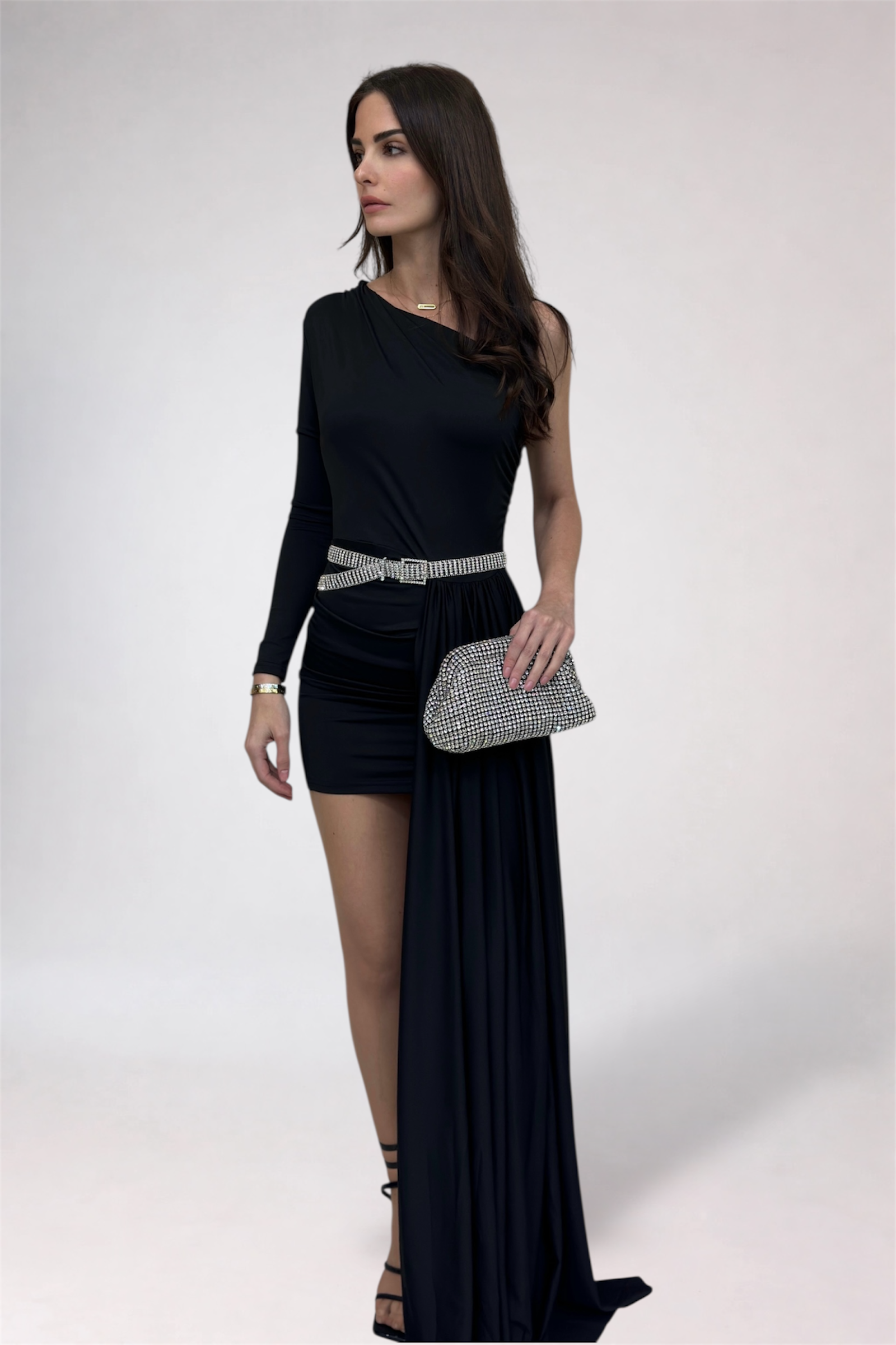 Woman wearing a black dress with a high slit, holding a clutch, on a white background