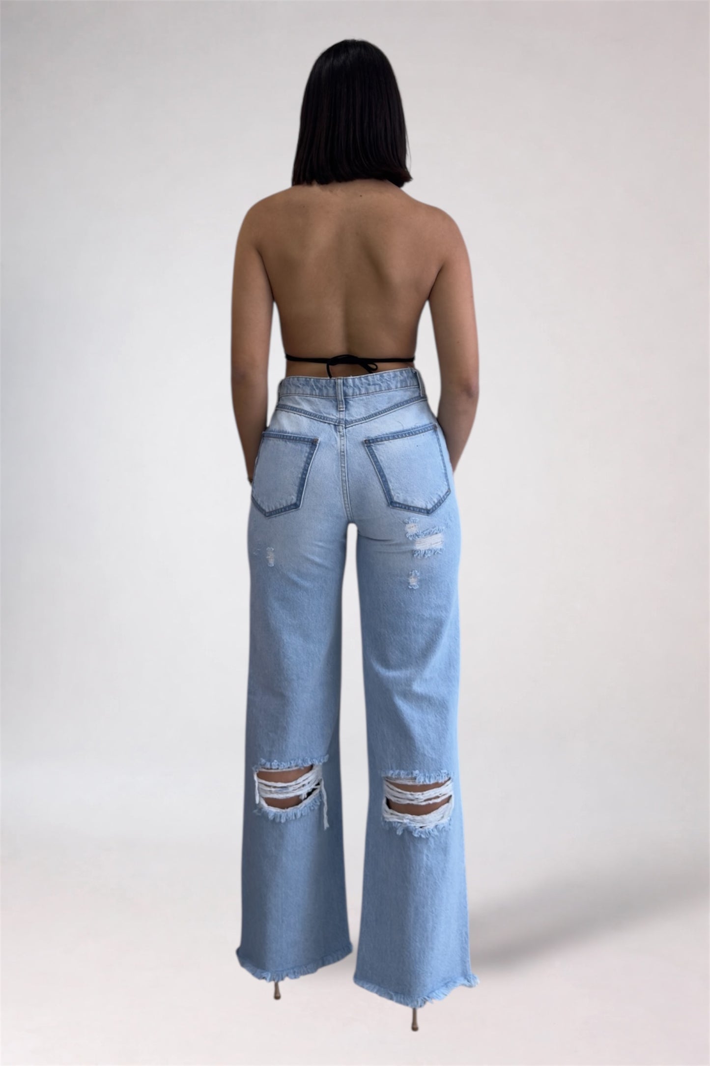 Person wearing light blue distressed jeans on a white background