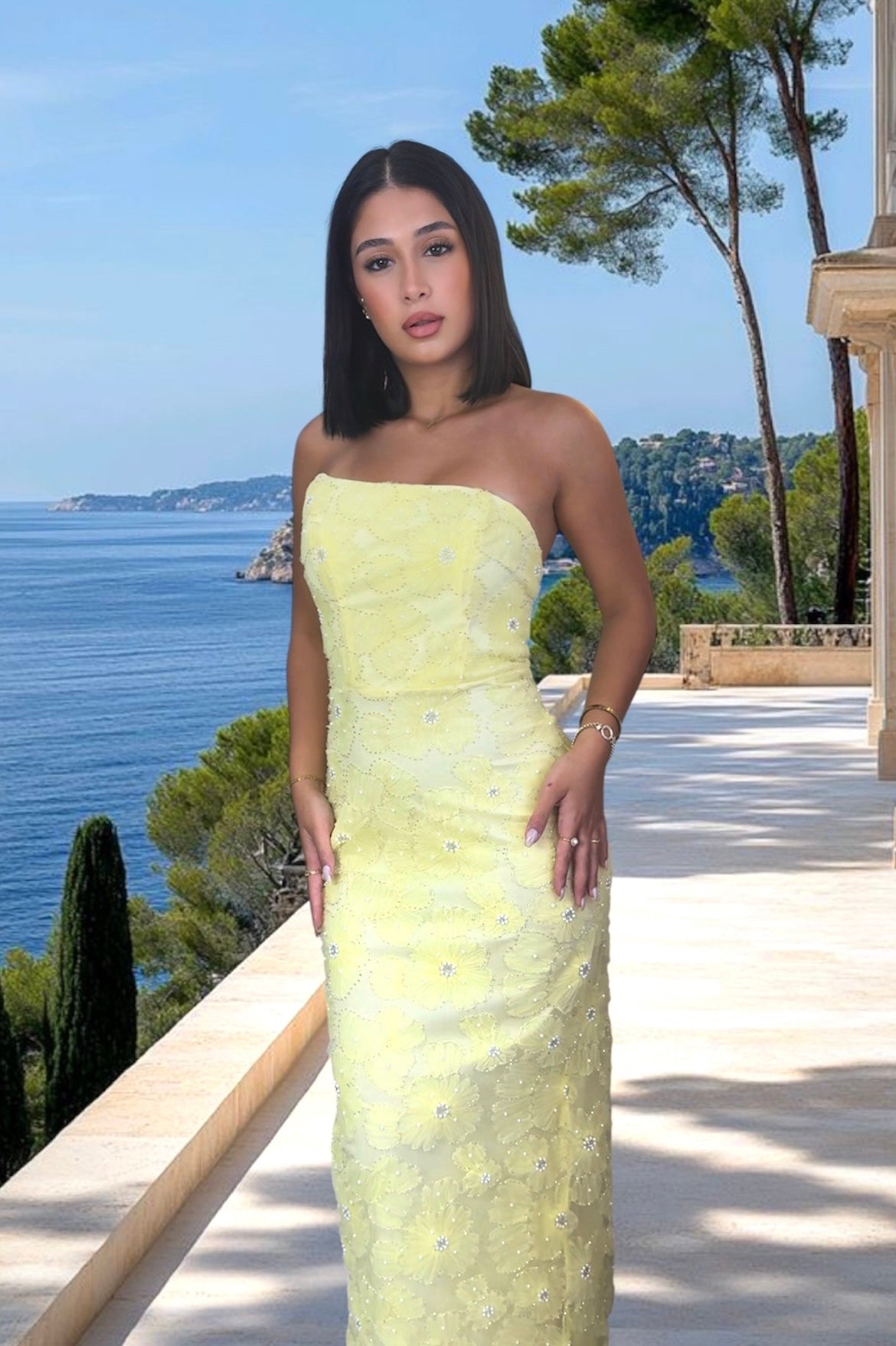 Woman in a strapless yellow dress standing on a balcony with ocean view
