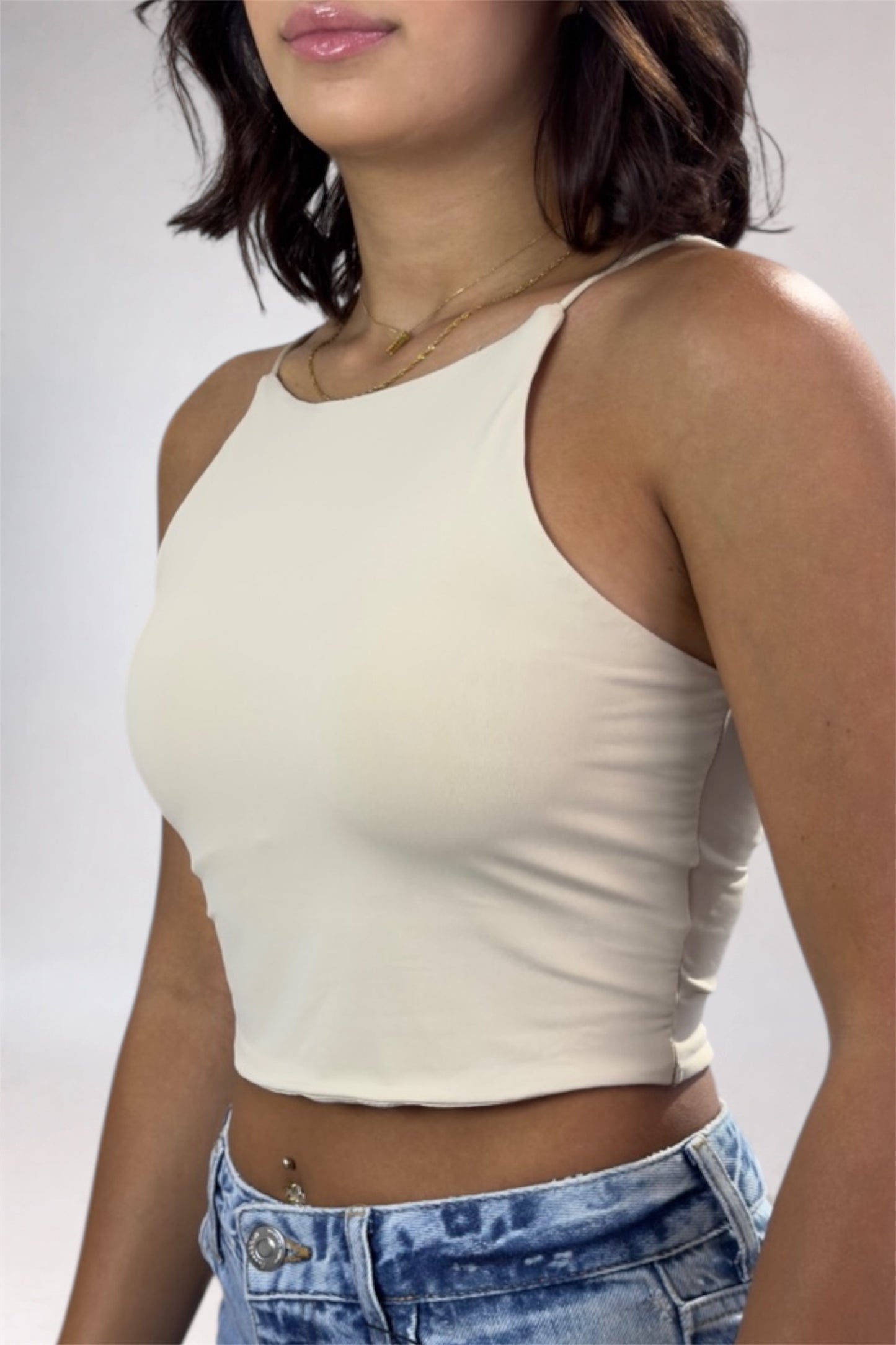 Woman wearing a beige tank top and blue jeans against a plain background