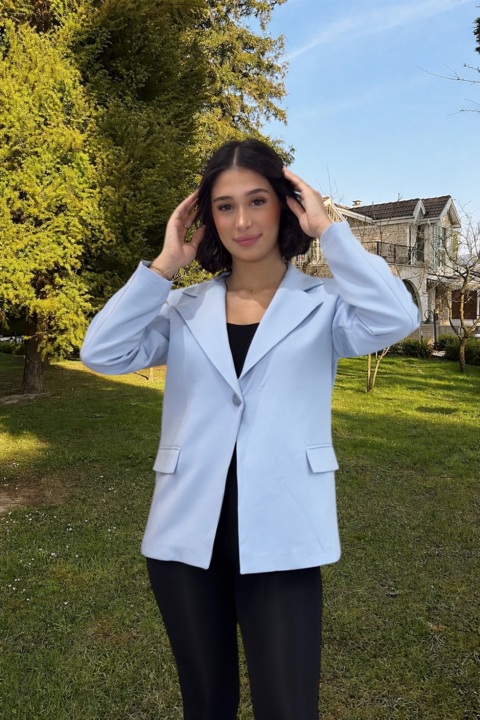 Woman wearing a light blue blazer outdoors with trees and a house in the background