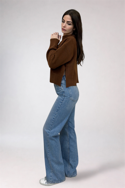 Woman wearing a brown sweater and blue jeans on a plain background