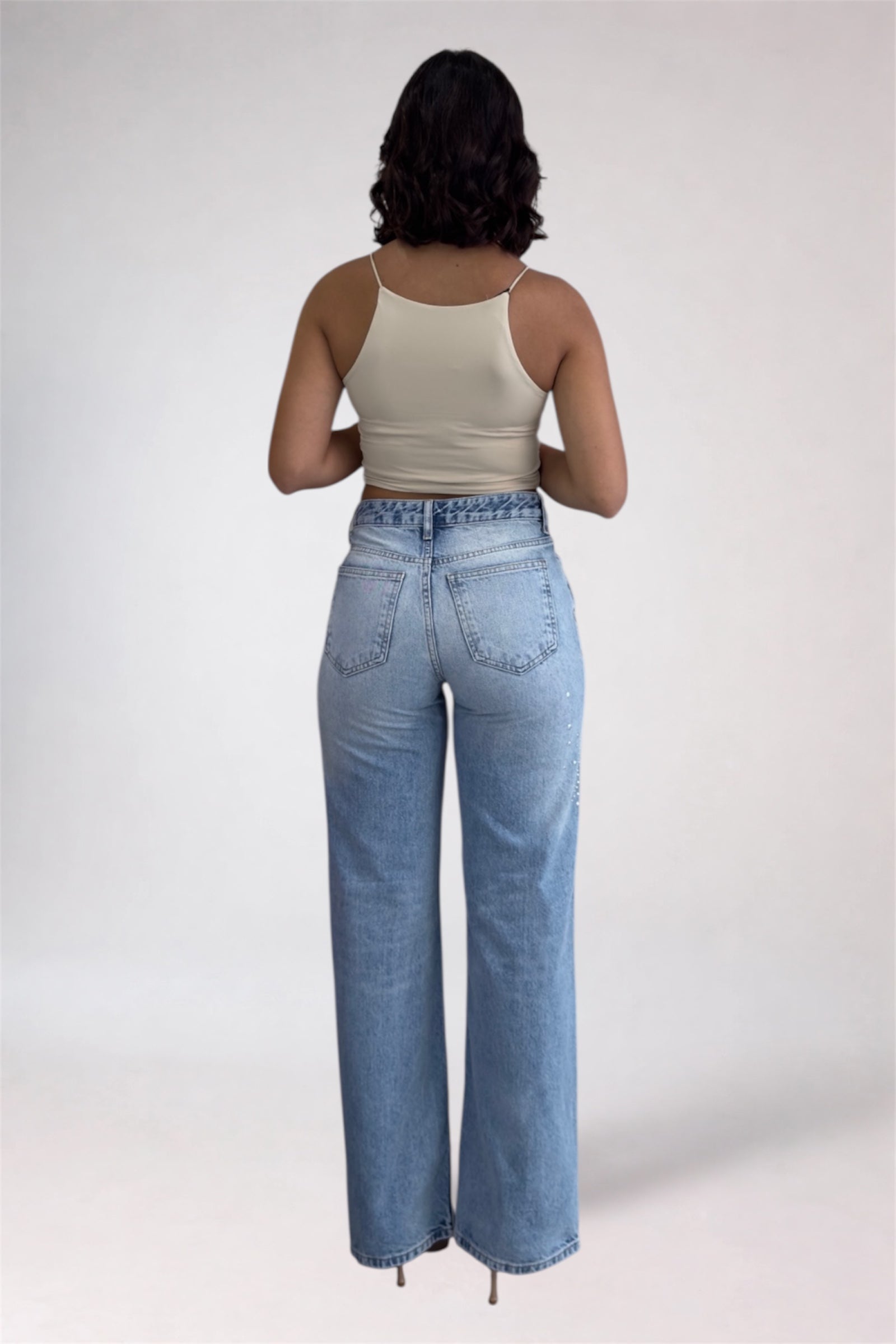 Person wearing light blue jeans and a beige top on a white background