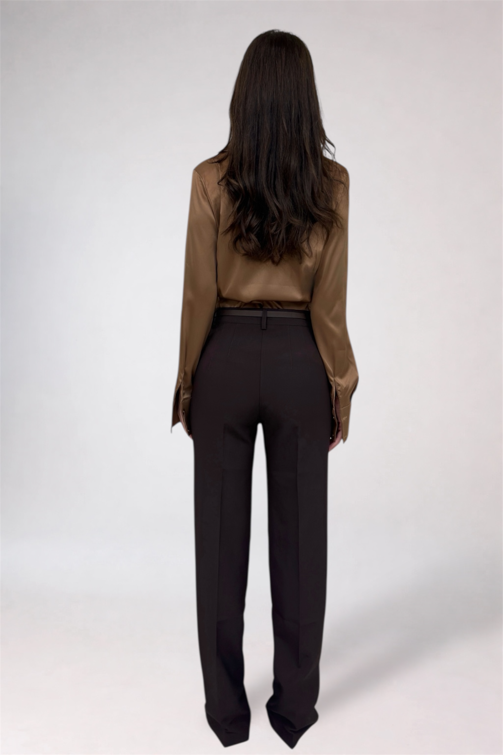 Person wearing a brown blouse and black pants on a white background