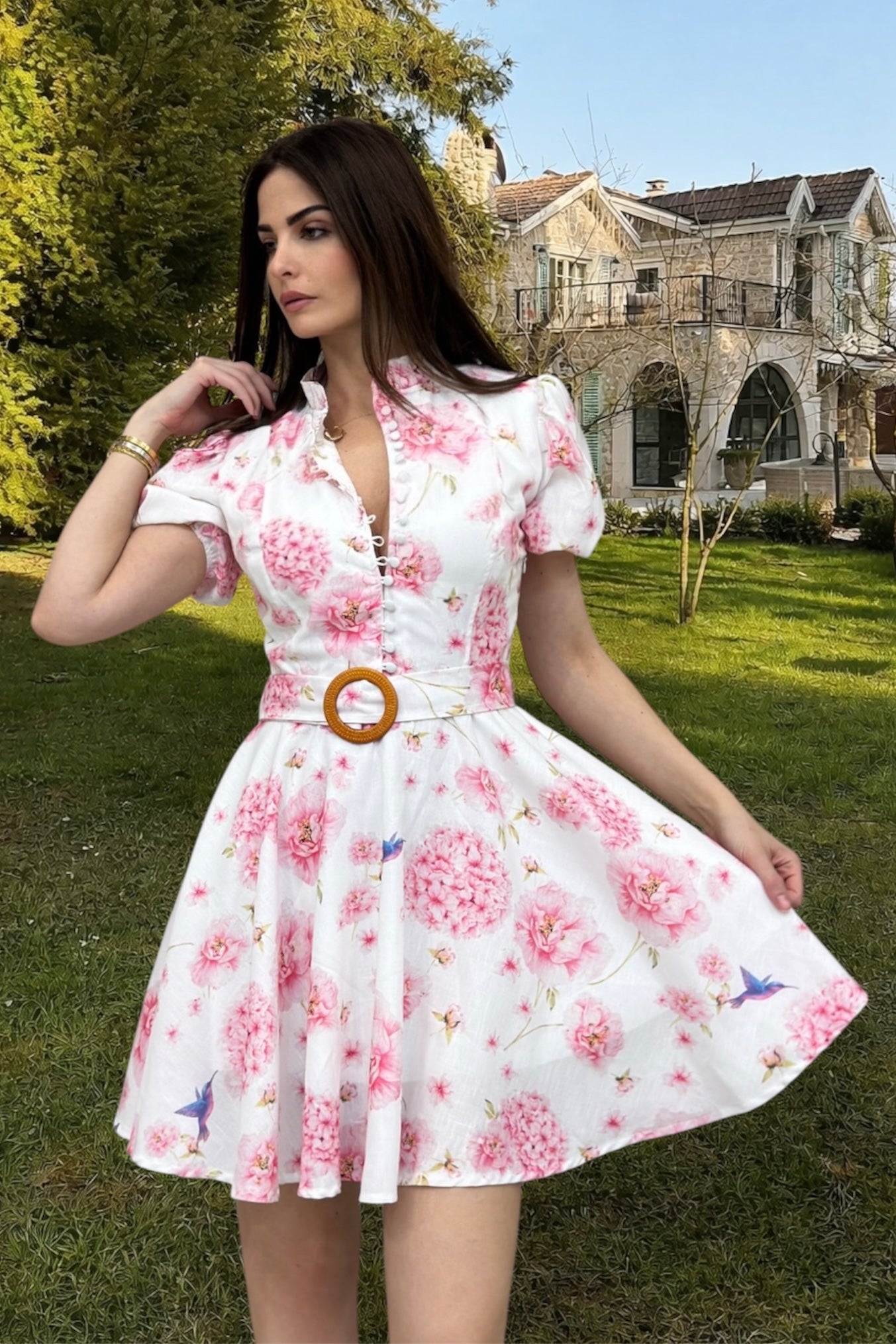 Woman wearing a floral dress with a wooden belt in an outdoor setting.