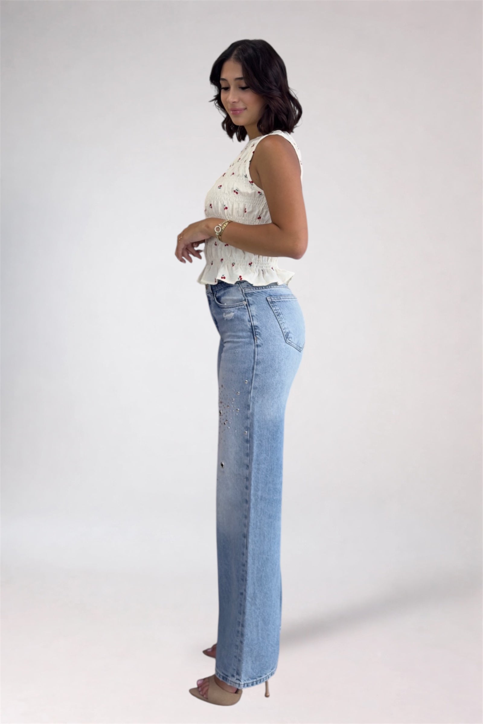 Woman wearing a white sleeveless top and blue jeans on a plain background