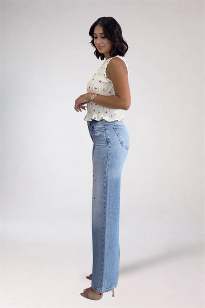 Woman wearing a white sleeveless top and blue jeans on a plain background