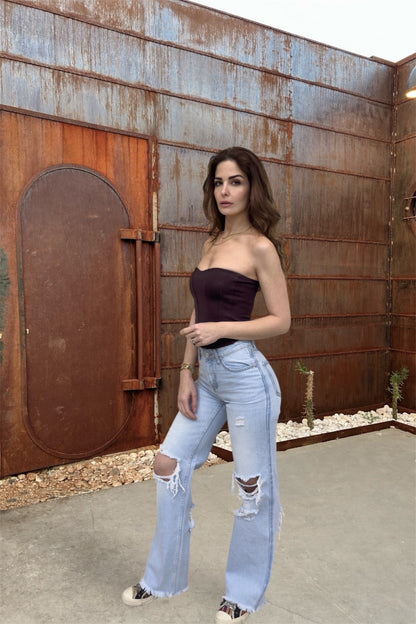 Woman in a strapless top and ripped jeans standing in front of a rusted metal wall.