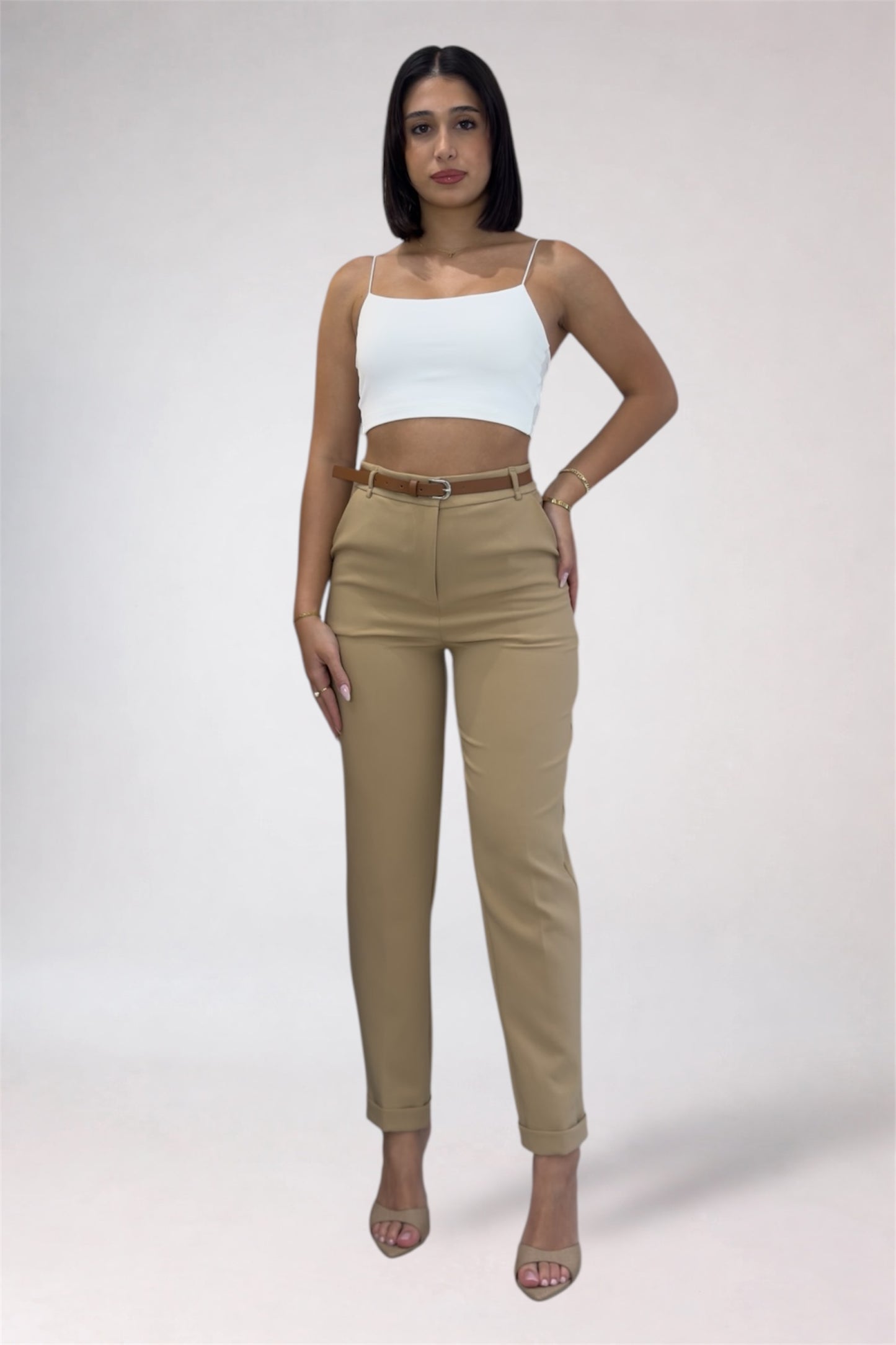 Woman wearing a white top and beige pants on a plain background