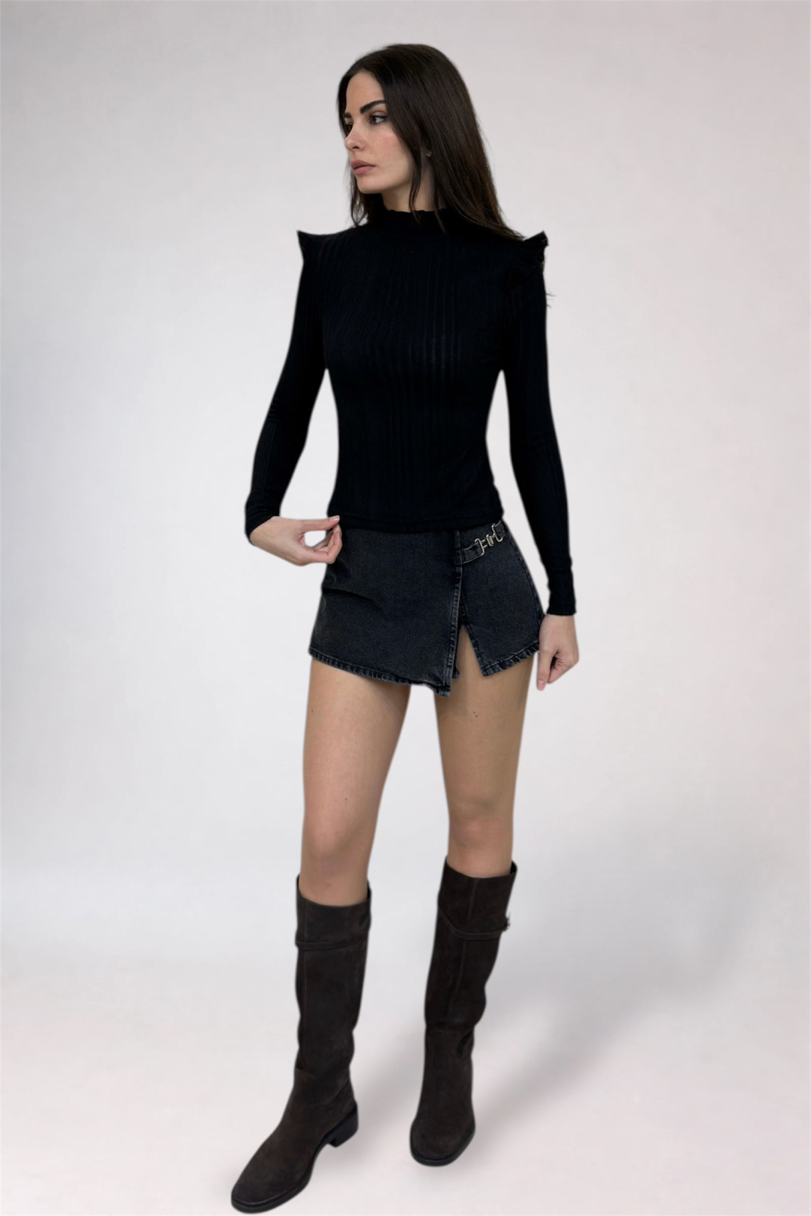 Woman wearing a black long-sleeve top and denim skirt with knee-high black boots on a white background