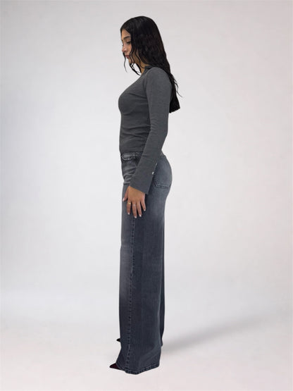 A woman shown in profile wearing a dark gray long-sleeve top and matching dark gray wide-leg jeans against a plain light gray studio background.
