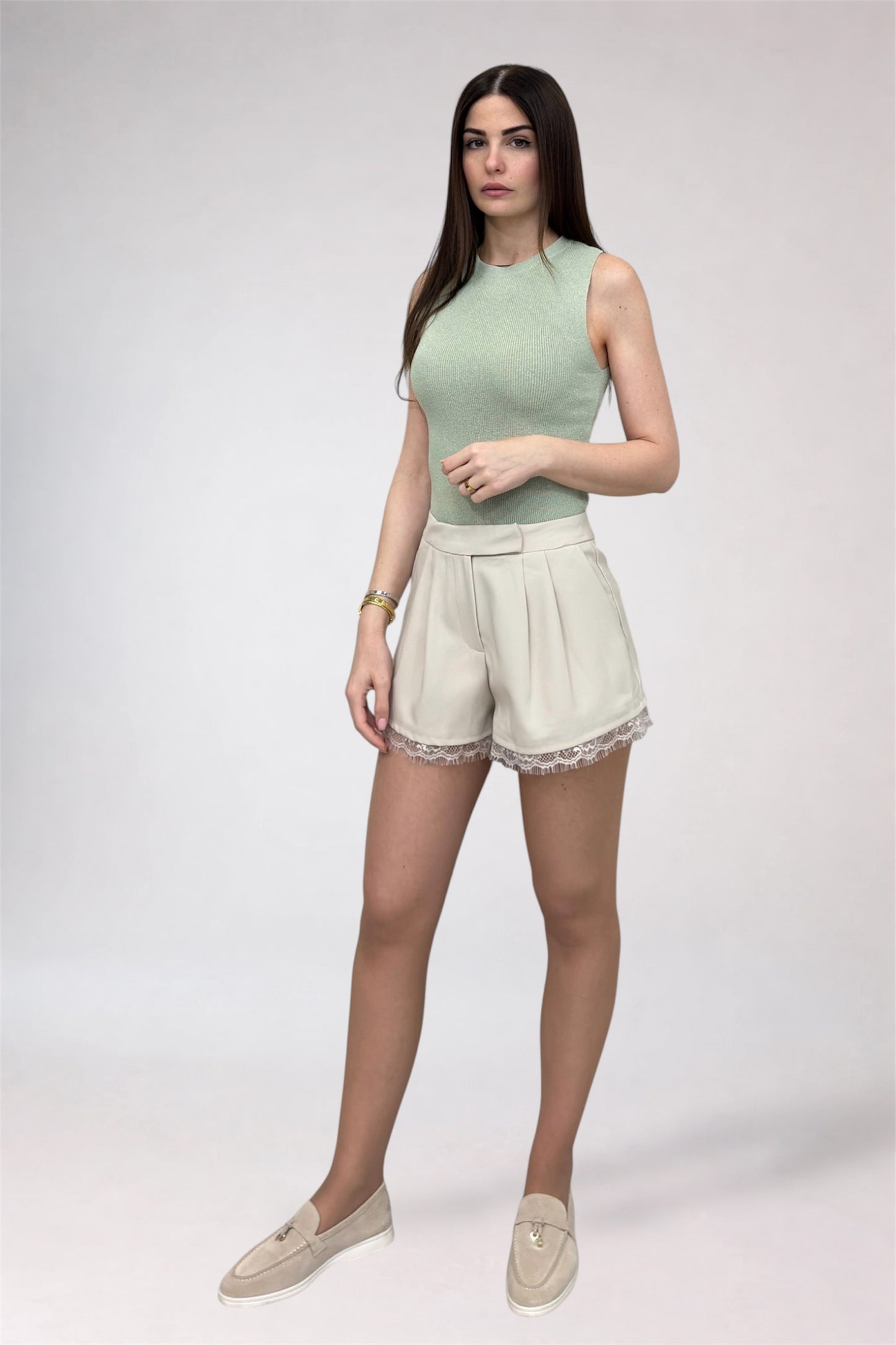 Woman wearing a light green sleeveless top and beige shorts on a white background
