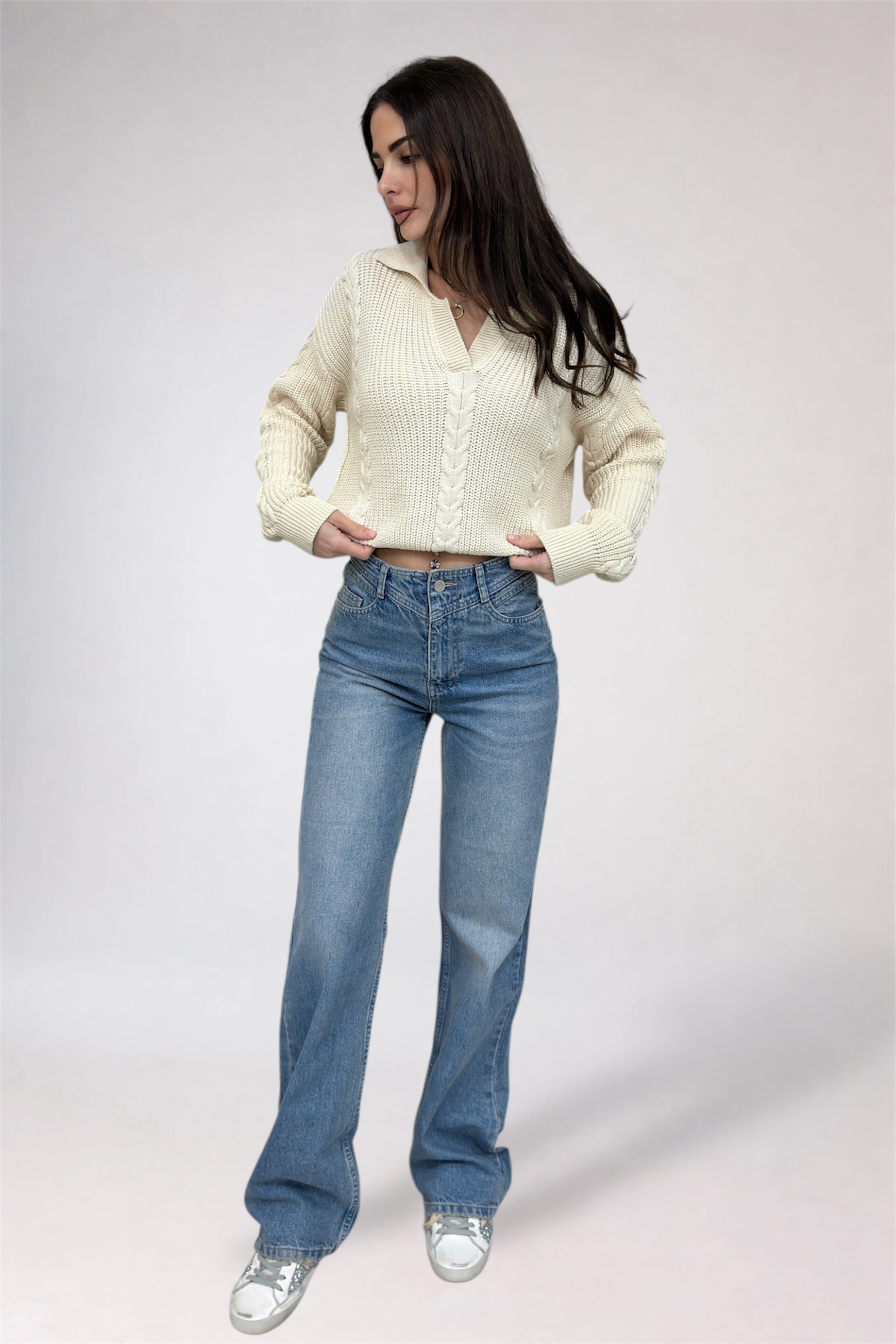 Woman wearing a cream cardigan and blue jeans on a white background