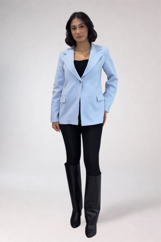 Woman wearing a light blue blazer over a black top and pants, standing against a white background.