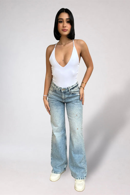 Woman wearing a white tank top and light blue jeans on a plain background