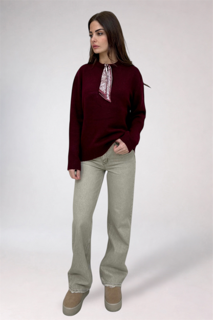 Woman wearing a burgundy sweater with lace details and light gray pants on a white background