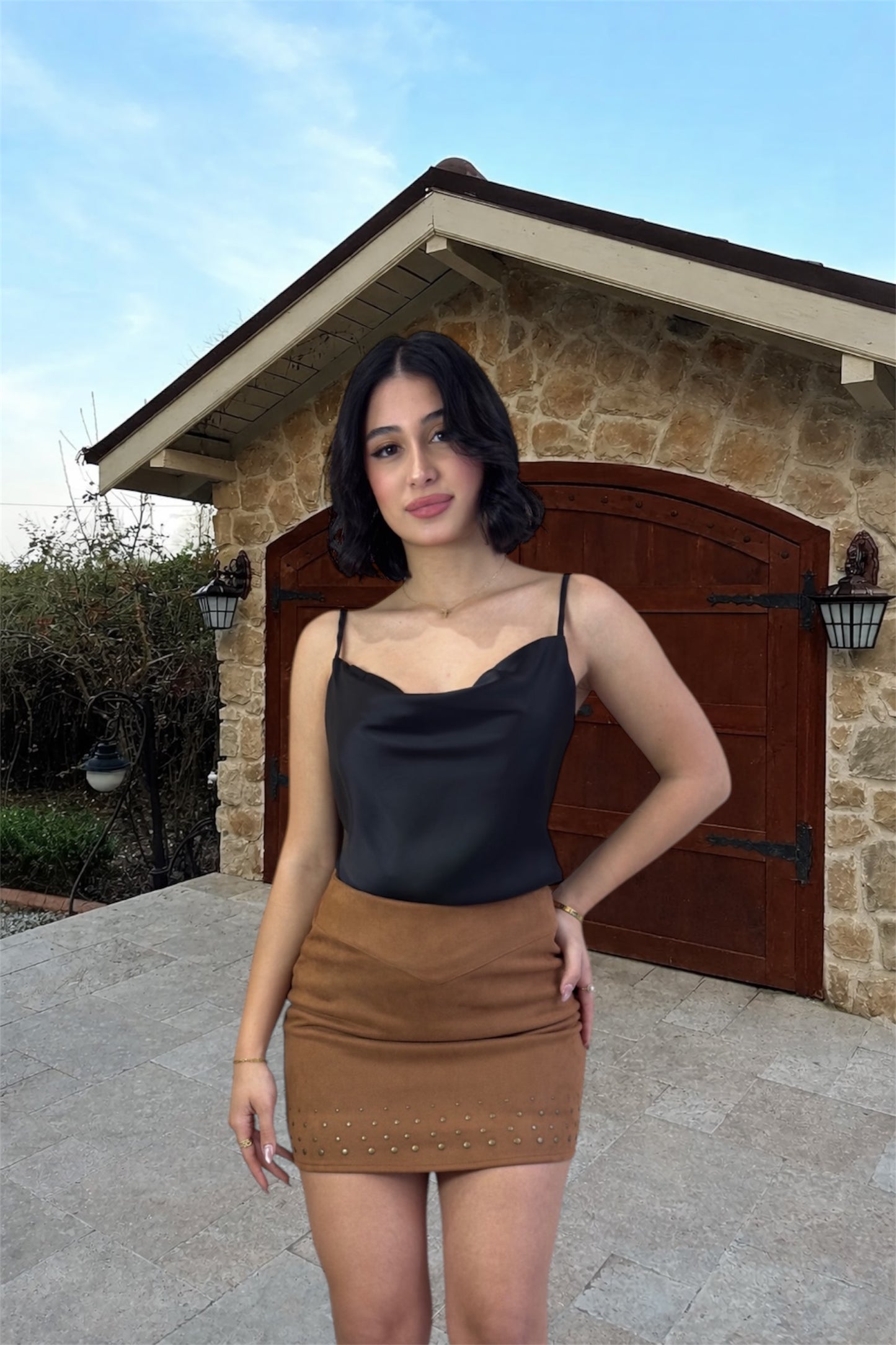 Woman in black top and brown skirt standing in front of a stone building with wooden door.