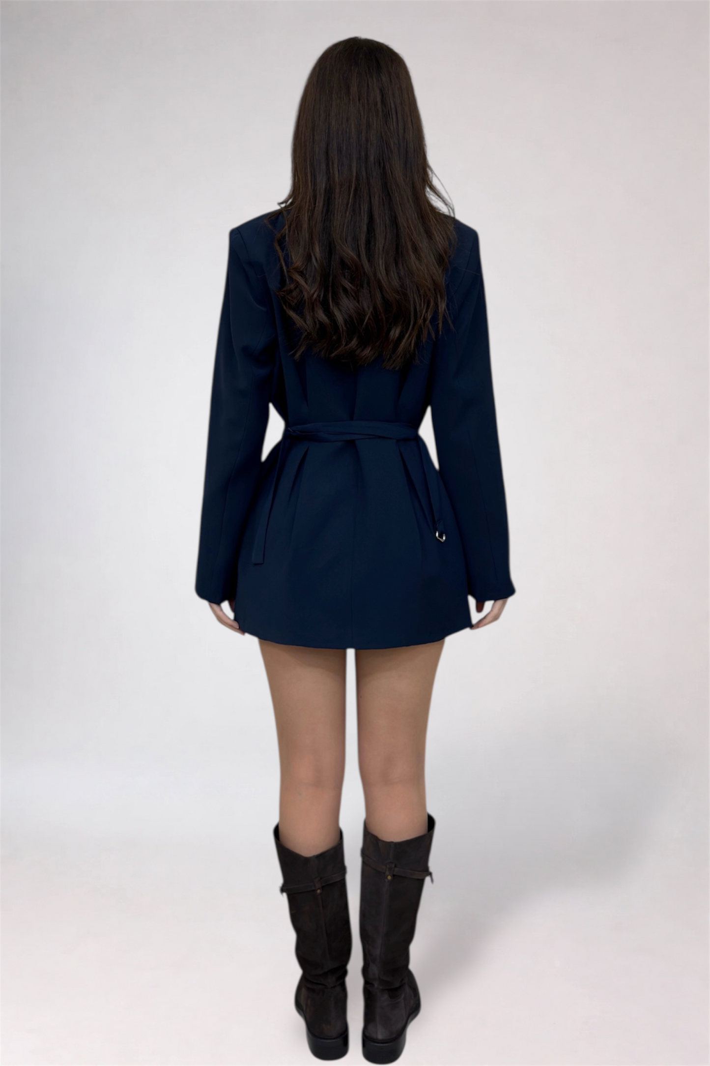 Person wearing a navy blue trench coat and black boots on a white background