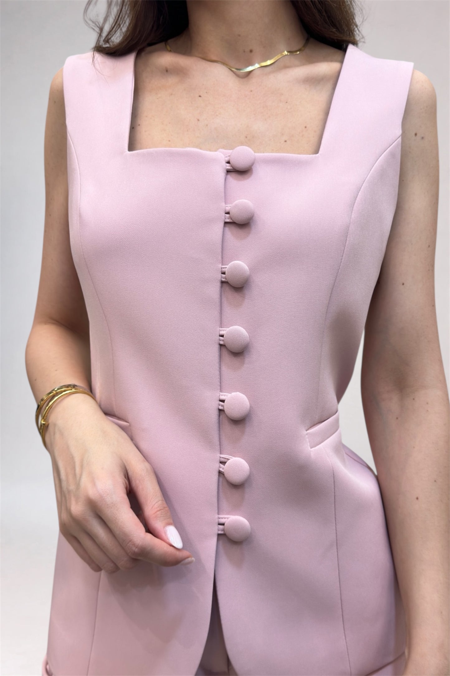 Pink sleeveless dress with button details on a plain background