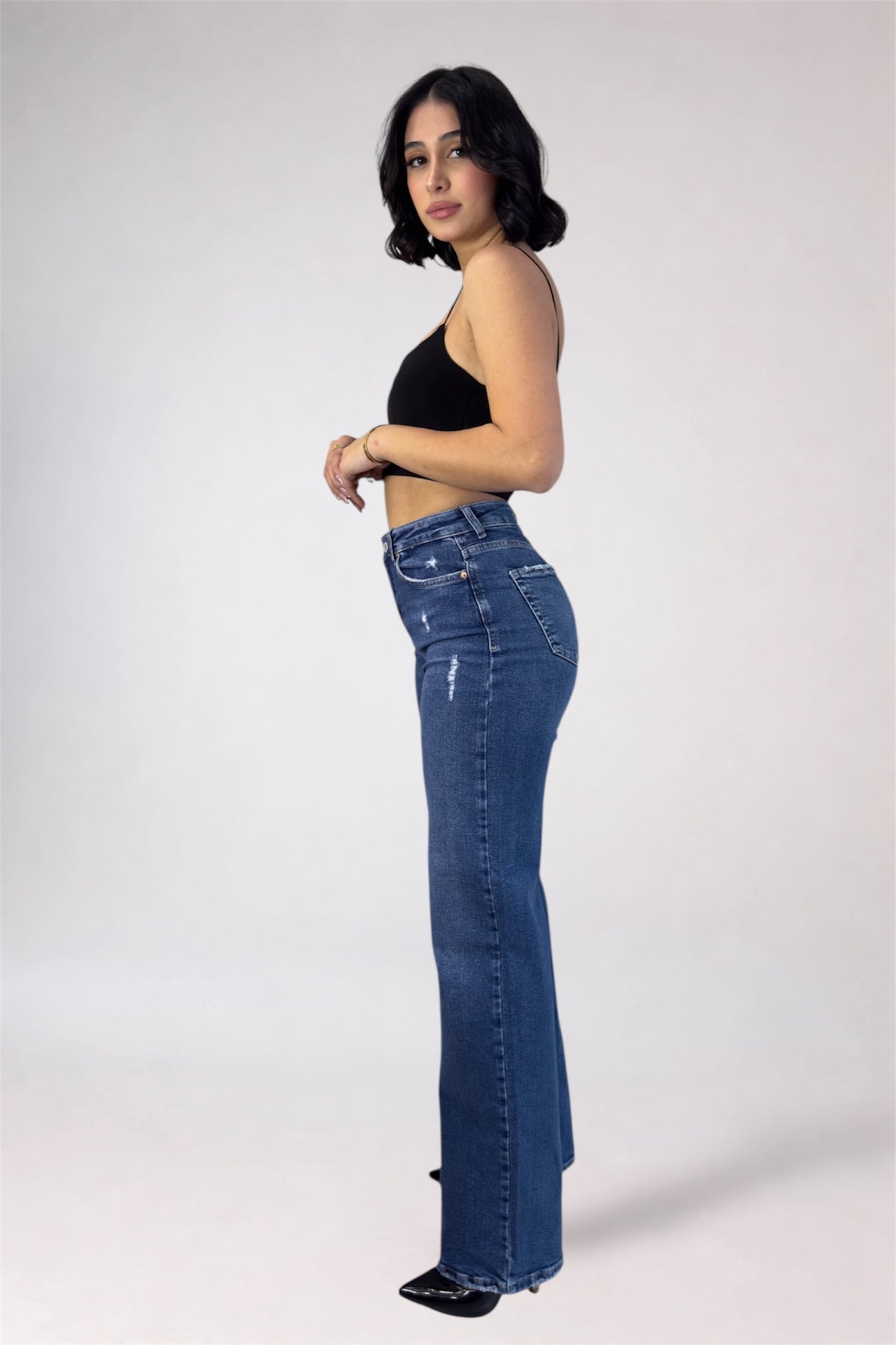 Woman wearing blue jeans and a black top on a white background