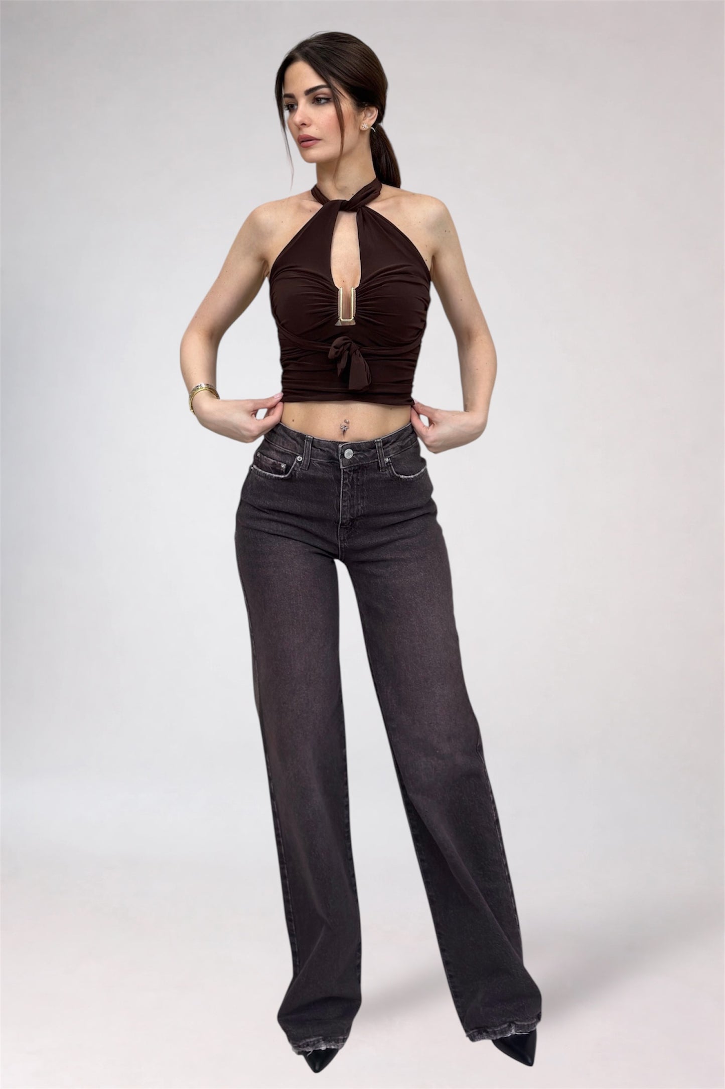 Woman wearing a brown halter top and black high-waisted jeans on a white background