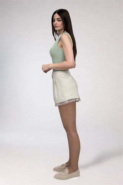 Woman wearing a light green sleeveless top and cream shorts on a white background