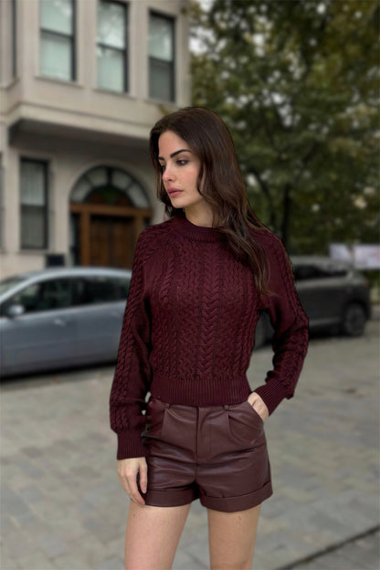 Woman wearing a maroon sweater and shorts standing on a street.