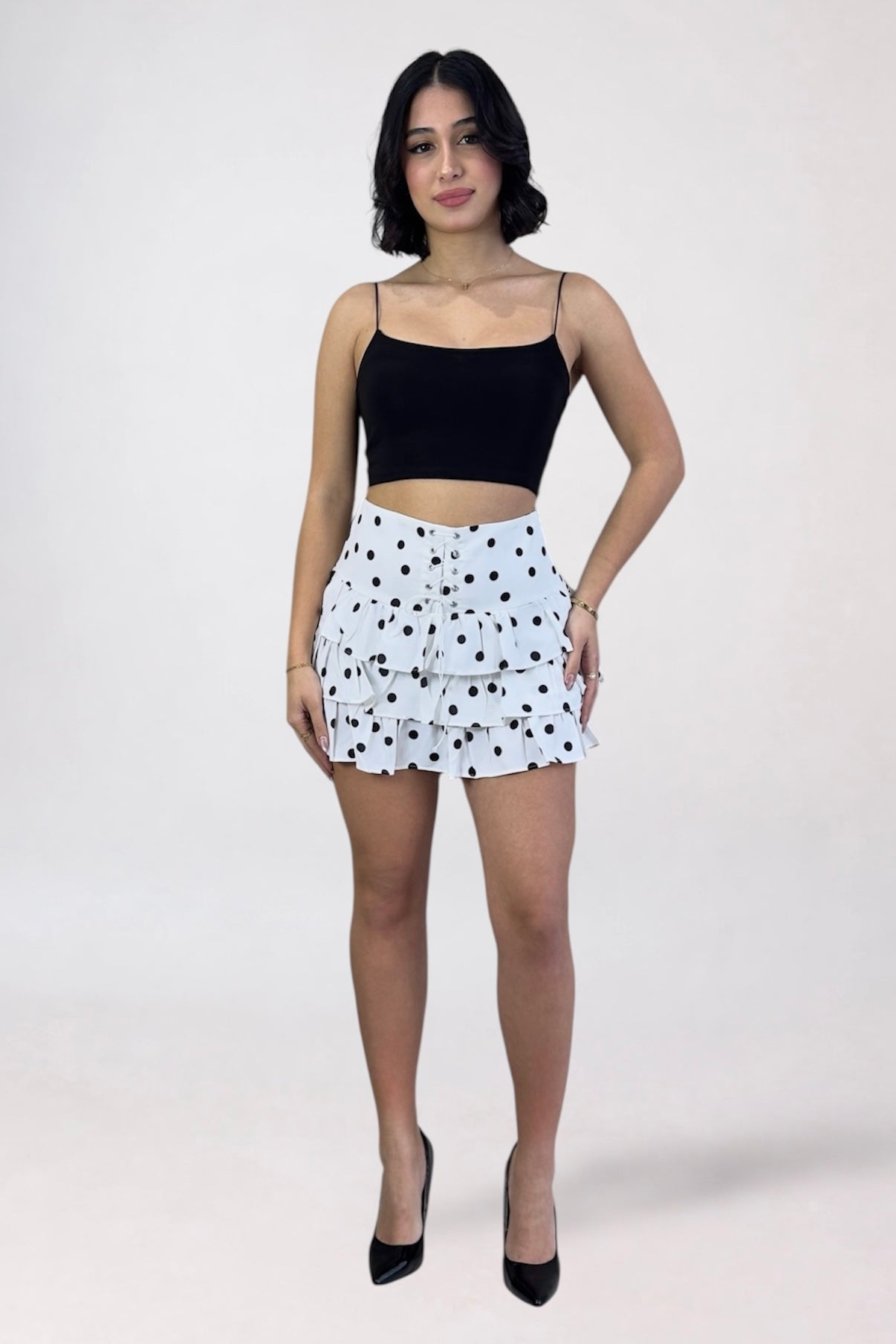 Woman wearing a black crop top and white polka dot shorts on a white background