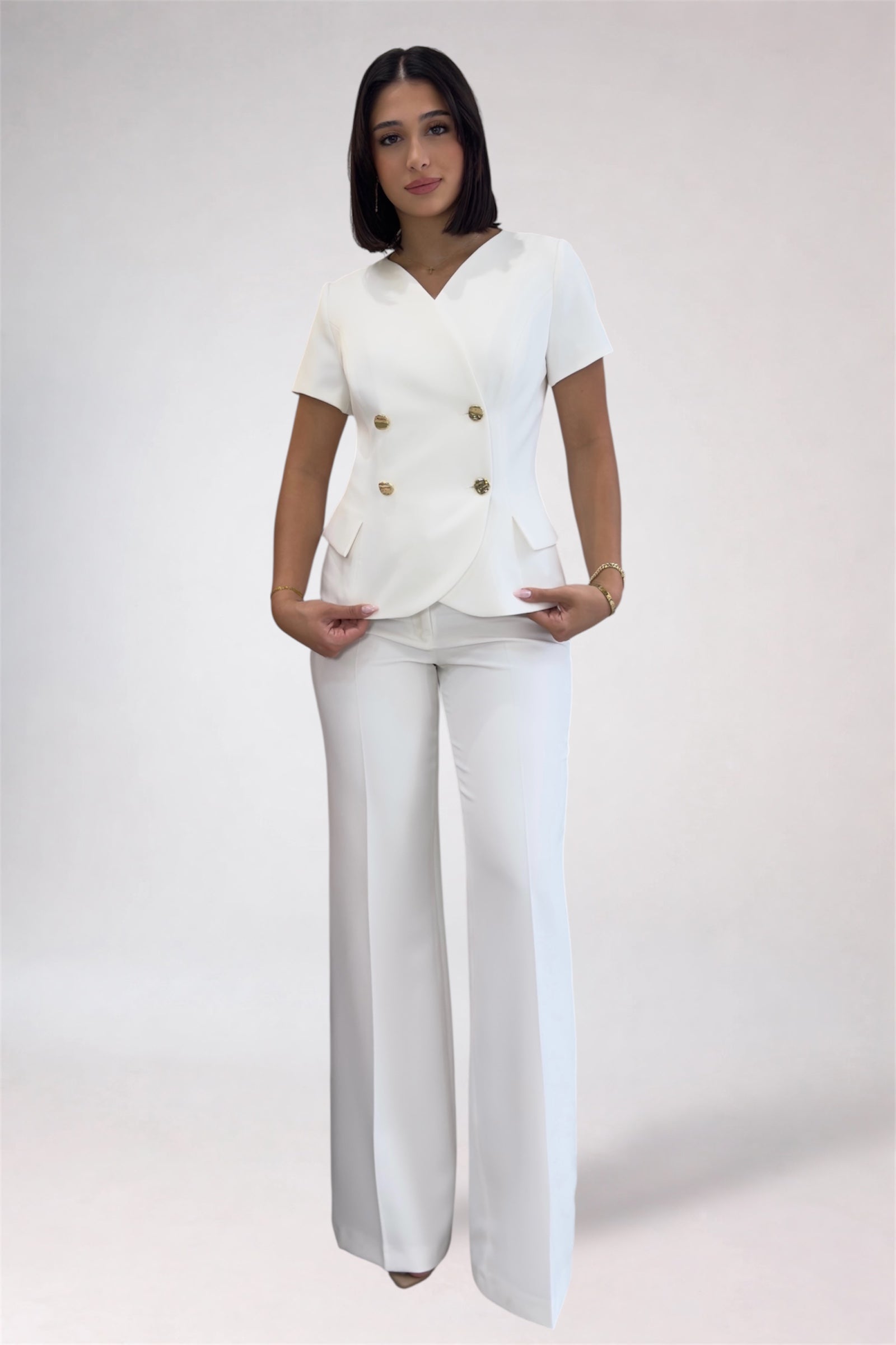 Woman wearing a white outfit with gold buttons on a plain background