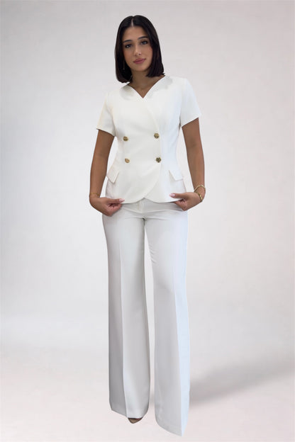 Woman wearing a white outfit with gold buttons on a plain background