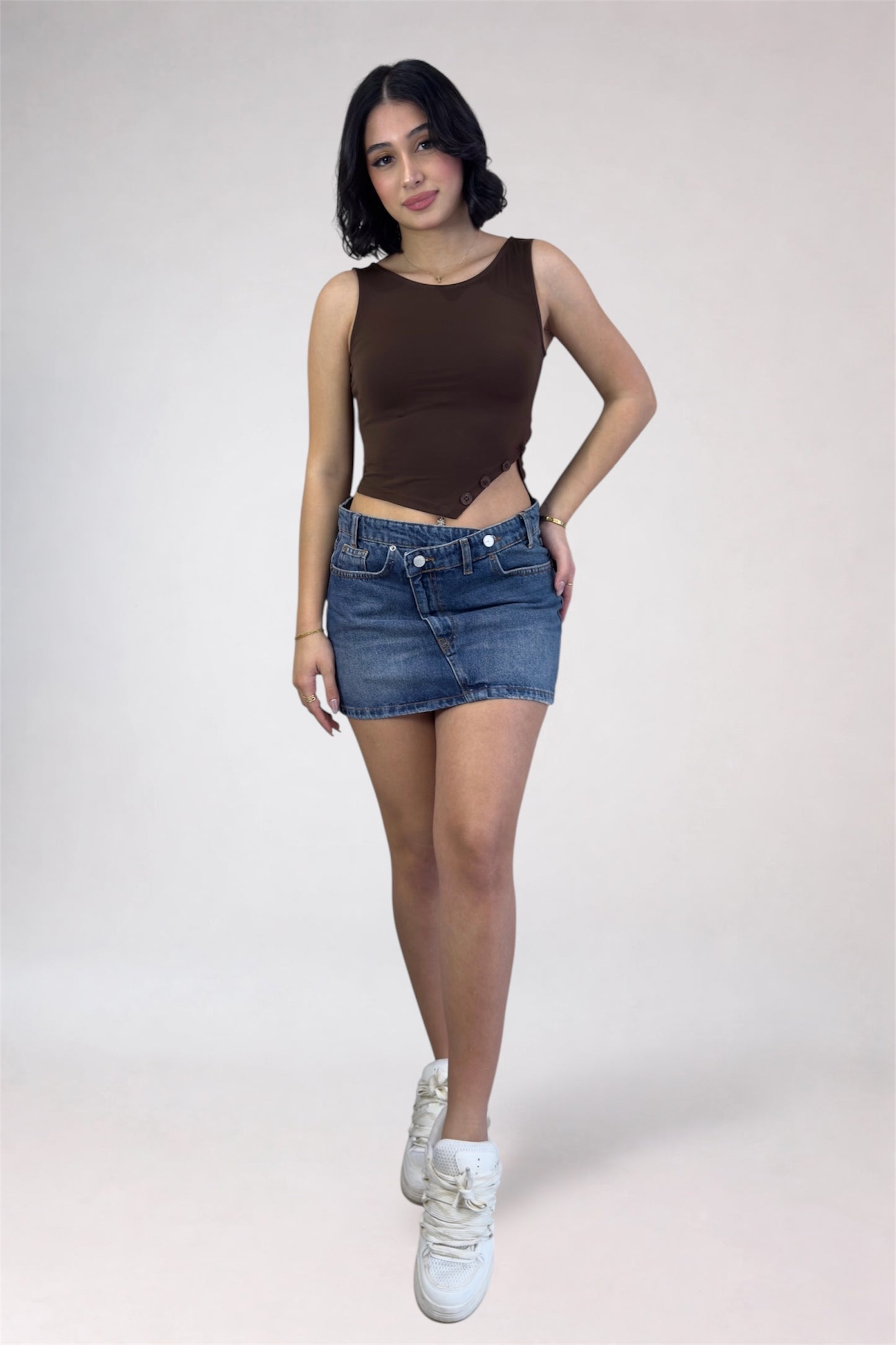 Woman wearing a brown sleeveless top and denim shorts on a white background
