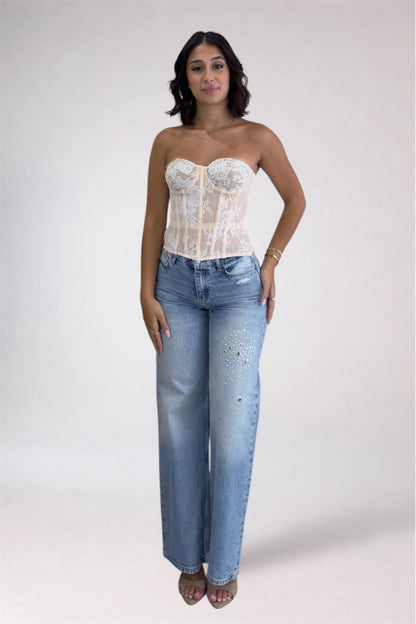 Woman wearing a white lace top and blue jeans on a plain background